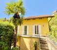2 story house, yellow paint, terracotta roof, balcony, stairs to entrance, greenery surrounding