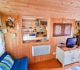 room with wooden walls, white desk, wooden floor, TV, couch with pillows, bed, night lamp