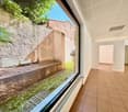 View from an open window to a backyard with grassy area, trees, brick path
