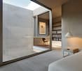 Modern, minimalist bedroom with large glass windows, sleek design, warm lighting, bed with pillows, nightstand, and lamp.