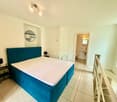 modern bedroom, teal bed, white walls, white bed linen, bedside table with lamp, open doorway leading to bathroom