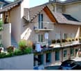 two-story house, tiled roof, several balconies, exterior steps, potted plants, cars parked in front