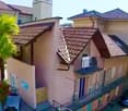 3-story house, brown roof, white walls, balconies, palm trees, cars parked