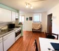 wooden floor, white cabinets, stainless steel sink, electric oven, lamps, chairs, desk