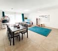 Dining table with chairs, white walls, beige floor, blue rug, white microwave, bookshelves, whiteboard, children's toys
