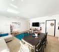 Dining room: table, 6 chairs, blue rug, sofa with blue cushions, white shelves, entertainment center with television, decorative items