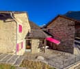 Stone building with red awning, pink shutters, stairs, metal railing, grassy slope, distant mountains