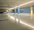 This image shows an indoor parking garage with a concrete floor, blue walls, and lockers along the side. There is a single car parked in the garage, and the space appears to be well-lit with overhead lighting.