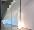 The image shows a modern interior with a glass wall, a white floor lamp, and a staircase visible in the background.