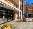 Commercial building with a glass storefront displaying various items and products, multiple plants for decoration, two apartment buildings with balconies, paved outdoor area