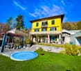 Large yellow house, wooden balcony, well-kept garden, pool, outdoor dining area, stone steps, lush greenery