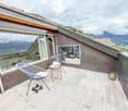 Decked balcony with chairs, table, and dumbbells, glass windows overlooking mountains
