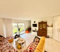 Open living room, large windows, white flooring, couch, television, table, exercise bike, wardrobe, small white cabinets