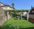 Stone wall, green lawn, picnic table, wooden bench, grapevines