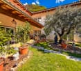 Garden with various potted plants, walking path, wooden pergola, statues, and green grass