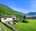 traditional alpine house, yellow walls, grey roof, mountain landscape, green lawn, wooden pergola