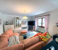 Spacious living room with large windows, pink and orange sofa, glass coffee table, TV stand, display cabinet, and colorful decorative pillows