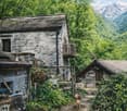 stone house, wooden balcony, surrounded by trees, mountains in the background