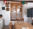 kitchen with dining area, wooden window, wooden chairs, table, white walls, wooden beams, Swiss flag