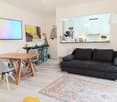 Living room with wooden table, chairs, couch, rug, TV, and kitchen area
