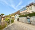 Houses on a cobblestone street, stone walls, hedges, and a hillside in the background.