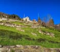 hill with green grass, stone wall, house in the background, mountain in the distance