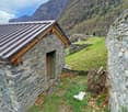 Stone house, metal roof, wooden door, surrounded by grass and mountains