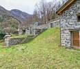 Stone house, raised ground floor, wooden door, stone walls, grassy slope, wooden fence, mountain view