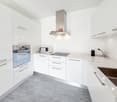 modern kitchen with white cabinets, gray floor, stainless steel appliances, microwave, oven, induction cooktop, sink, and a stainless steel chimney hood