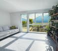 modern living room with large windows, gray couch, green pillows, tiled floor, large plant shelf