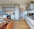 modern kitchen with wooden floor, gray cabinets, wooden dining table, brown chairs, open door, appliances, plants