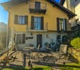 2 story house, yellow exterior, black shutters, balcony, patio with table and chairs, potted plants