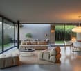 Spacious open-plan living area with large glass sliding doors leading to a terrace or balcony, providing a scenic view of the outdoor greenery. The room features a comfortable L-shaped sofa, a round coffee table, and a dining area with a wooden table and
