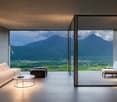 Spacious living room with large windows offering a stunning view of the mountainous landscape. The room features a comfortable sofa, a coffee table, and an armchair. The minimalist and modern design creates a serene and relaxing atmosphere.