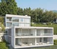 Modern, multi-story house with large glass windows and balconies, surrounded by lush greenery and trees