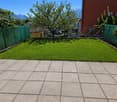 well-maintained garden with green lawn, surrounded by green fences, paved patio, trees, and plants