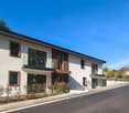 2-storey building, white exterior, brown trims, glass windows, balconies, garden in front