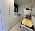 A small room with white cabinets, sink, washing machine, and a window.