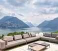 Outdoor seating area with two couches, a coffee table, and a glass railing overlooking a lake and mountains.