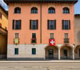 Three story building, beige and orange walls, multiple windows, Swiss flag on the front