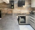 modern kitchen with gray countertops, wooden wall, black oven, gray chairs, gray cabinets