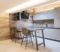 modern kitchen with wooden table, two stools, wooden wall, gray cabinets, sink, faucet, TV