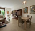 Large room with couch, wooden table, dining chairs, bookshelf, glass door, windows, framed paintings