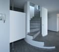 Entrance hall, spiral staircase, white walls, gray flooring, glass elements, telephone mounted on the wall, cabinet in the hallway