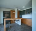 large island countertop with stools, modern open-plan kitchen, wooden cabinets, stainless steel appliances, white walls, gray floors
