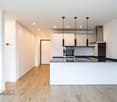 Modern kitchen with black countertops, white cabinets, wooden floor, hanging lamps, a sink with a faucet, an oven, an extractor hood, and a white central island.