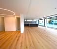 Spacious open-plan living area with hardwood flooring, large windows providing natural light, and a balcony or terrace visible.