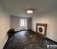 Large room with gray walls, hardwood floor, and a fireplace with a decorative frame. There is a wooden desk and a framed artwork on the wall.