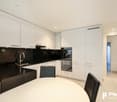 Modern, open-plan kitchen with white cabinets, black countertops, stainless steel appliances including a dishwasher, and a round dining table with black chairs.