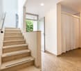 The image shows the interior of a residential property. It features a staircase with beige marble steps leading up to the second floor. The hallway has white walls and a curtain-covered doorway leading to another room. The floor is covered with a light-co